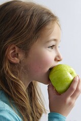 A young girl enjoying a healthy snack by taking a bite out of a crisp, green apple.