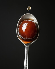 Gulab Jamun Served on a Spoon With Syrup Droplet in Low Light Setting