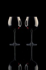 Elegant wine glasses with ruby-red liquid reflected in a dark, mirrored composition. A sophisticated and moody still life