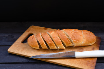 Freshly baked bread sliced on a wooden cutting board with a sharp knife beside it