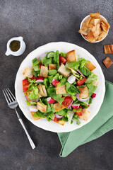 Fattoush salad with fresh vegetables and crispy toasted pita on grey background. Top view. Lebanese cuisine.