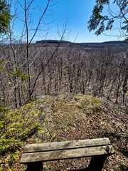 A wooden bench at a remote trail hiking path lookout on a rocky hill, a view over a forest in the...