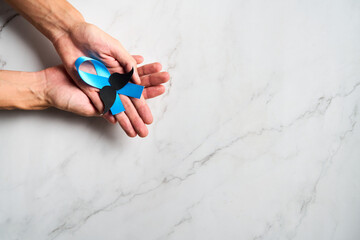 Hands holding Blue ribbon with mustache supporting prostate cancer awareness month and men's health