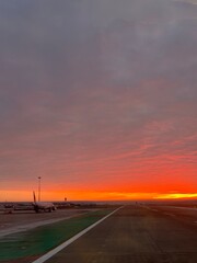 Snowy Airport Runway at Red Sunrise with Distant Plane. Bright red sunrise over a snowy airport...