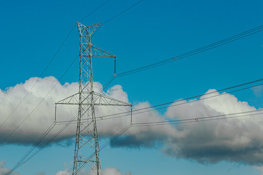 Steel lattice transmission towers supporting high voltage power lines under a bright blue sky with scattered clouds.