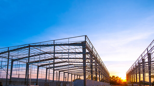 Silhouette of industry warehouse factory building framework with metal structure in construction site against sunset sky background, low angle view with copy space