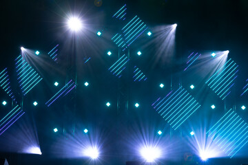 Bright purple and blue stage lights illuminate geometric arrangements of LED panels against a dark...