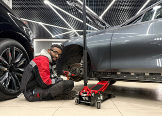 An African-American tire fitter with a wrench in his hands while working. The tire fitter removes...