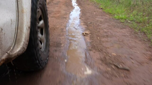 acercamiento de la llanta de un carro rodando por un charco de agua por un camino de lodo al aire libre salpicando tierra 