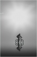 Obraz premium silhouette of a cyclist riding a bike with reflection on water at sunset
