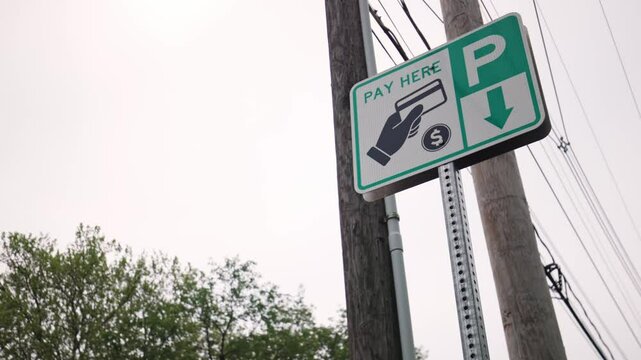 Pay here parking meter sign and station for car drivers to add payment for time spent parked in city public park area along sidewalk and road near downtown Columbus, Ohio in United States