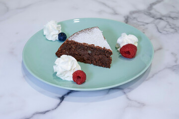 A slice of chocolate cake with whipped cream and raspberries on a green plate. The cake is cut in half and the whipped cream is spread on top