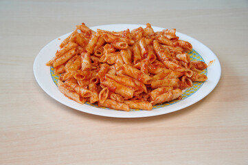 A plate of pasta with red sauce. The plate is white and blue