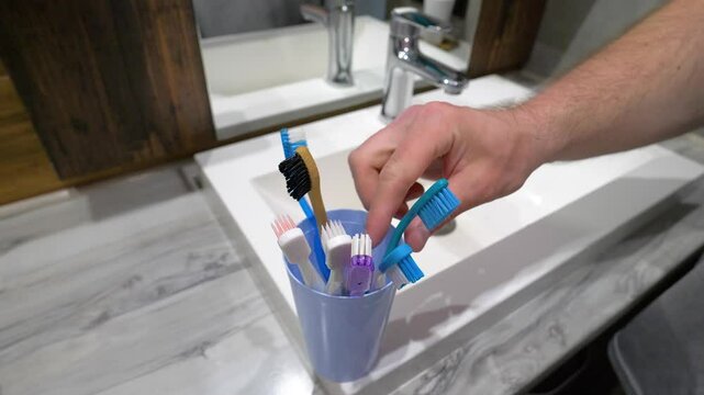  Close up, hand taking toothbrush, young man brushing teeth in bathroom at home. Slow motion