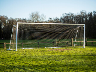 A soccer field with a goal and a fence in the background. The sky is cloudy and the grass is green. Football training ground. Popular outdoor sport. Nobody.