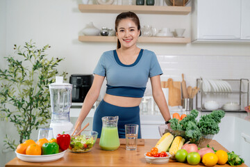 Young woman preparing healthy green smoothie with blender and fresh ingredients in kitchen