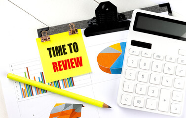 Sticky note with phrase time to review attached to financial documents with pie charts, bar graphs,...