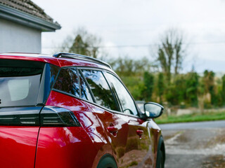 Red car parked outside house, small rural road and country side green area in the background....