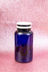 Blue plastic medicine bottle with white lid on pink glitter background