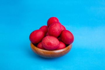 Red boiled easter eggs pile in a wooden bowl on blue background with copy space