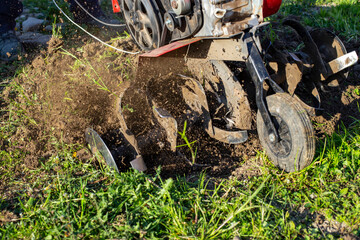 Garden tiller for cultivating field, loosens soil. Handheld motor plow throwing dirt with motion...
