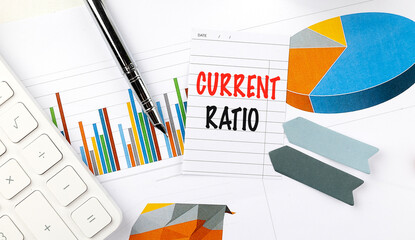 Card with the words current ratio placed on financial graphs and surrounded by office items and a calculator