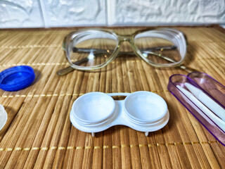 Clear glasses and contact lens accessories arranged on a soft fabric surface for daily eye care routine