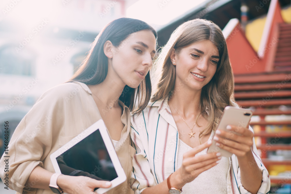 Poster attractive hipster girls reading received notification for smartphone gadget discussing mobility inn
