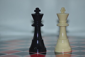 Black and white king chess pieces positioned side by side on a red and black checkered board,...