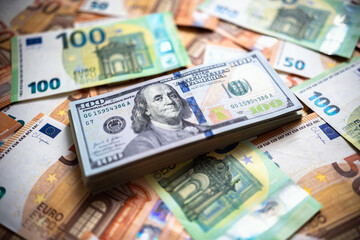 A stack of hundreds of American dollar bills is on top of euro money banknotes. Monetary background