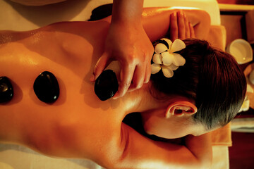 Closeup hot stone massage at spa salon in luxury resort with warm candle light, blissful woman...