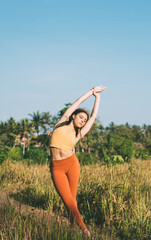 Caucasian female in track suit practise yoga outdoors on meadow enjoying sunny day and standing in asana, calm tranquil woman meditating and breathing feeling relaxation and body health balance