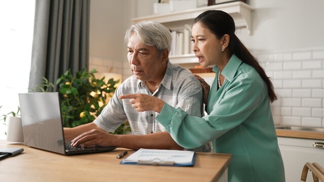Grandmother comforting and encouraging senior smart manager working and pointing at laptop showing deceasing financial chart. Elder couple helping and talking together while sitting at home. Myrmidon.