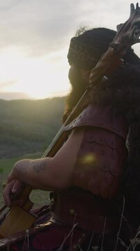Resting man in shaman clothes sits leaning on ikili in mountain valley at sunrise. Participant of folk rock band. Altai culture and traditions