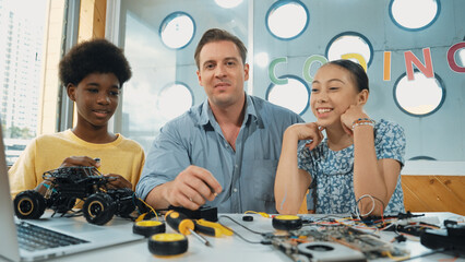 Teacher explain about electronic equipment while student with mixed races fixing car model at table...