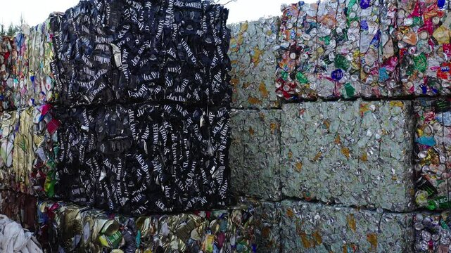 Stacks of crushed aluminum cans, including branded ones like Jack Daniel&rsquo;s, tightly baled for recycling at an industrial waste sorting site.
