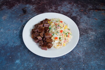 A plate of meat and rice. The meat is cut into small pieces. The rice is mixed with vegetables
