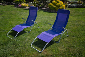 Two blue lounge chairs on a green lawn in a sunny garden
