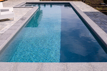 L-shaped pool is finished with a gray border stone. Clear blue water in the pool. Relaxing in the...
