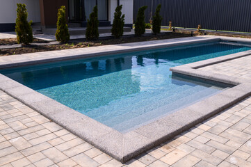 L-shaped pool is finished with a gray border stone. Clean blue water in the pool. Steps for a smooth descent into the water. Relaxing in the backyard of a country house