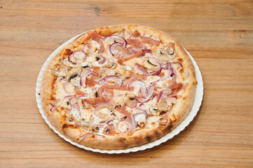 A pizza with mushrooms and onions on a white plate. The pizza is sitting on a wooden table