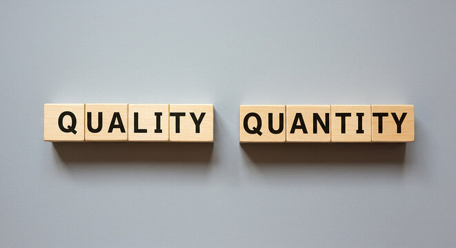 Wooden blocks spelling quality and quantity on a gray background in a studio shot overhead view