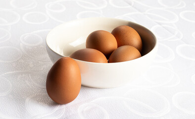 Four brown eggs in a bowl and one resting on the rim, white background.