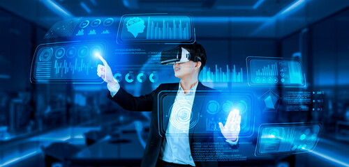 Project manager with VR goggles pointing financial chart and glowing blue light at office. Skilled...
