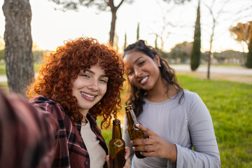 Two joyful multi ethnic female friends enjoying a sunny afternoon in the park, taking a selfie...