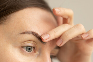 Woman takes off piece of dry skin from eyebrow after permanent makeup. Closeup. 