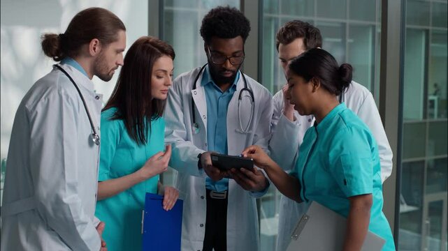 Multicultural five diverse people Caucasian Indian African women men doctors nurses looking digital tablet device examining together consulting health help diagnostic advice standing hospital hallway