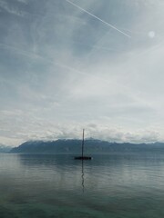 A sailing boat on the lake with snow-capped mountains and clouds in the background