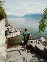 A boy walks down the stairs leading to the lake between the snowy mountains of Switzerland.
