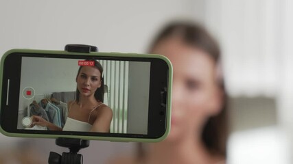 Young social medial content creator woman make fashion video. Blogger smiles to camera using selfie stick and light ring while making persuasive online clothing sell vlog to audience or follower. Adit